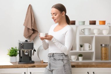 Mutfakta bir fincan sıcak kahve ve modern kahve makinesiyle güzel genç bir kadın.