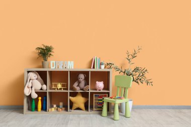Çocuk odasının içinde raflama ünitesi ve turuncu duvarın yanındaki sandalye.