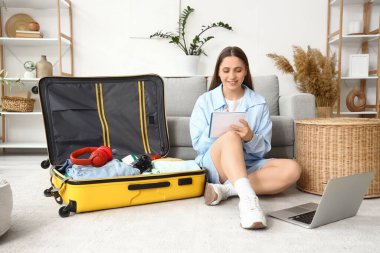 Evde bavul hazırlarken dizüstü bilgisayarlı kadın turist kontrol listesi yapıyor