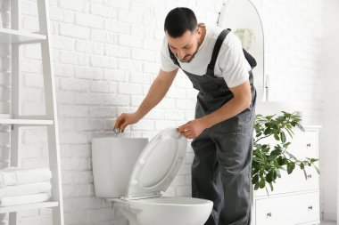 Erkek muslukçu, tuvaletteki klozeti tamir ediyor.