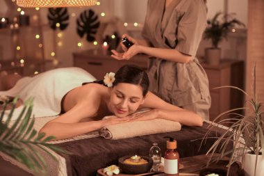 Genç bir kadın koyu renk spa salonundaki terapistin sıcak taşlar ve yağıyla masaj yaptırıyor.