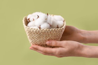 Yeşil arka planda pamuk çiçekli hasır kutu tutan kadın eller, yakın plan