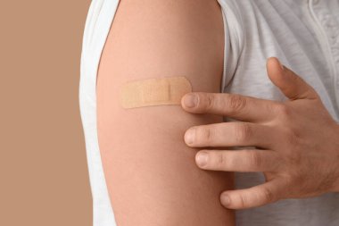 Bej arkaplandaki aşıdan sonra uygulamalı tıbbi yaması olan genç adam, yakın plan.