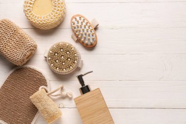 Beyaz ahşap arka planda masaj vücut fırçaları, süngerler ve bir şişe kozmetik ürünü ile kompozisyon, yakın plan