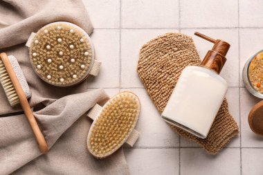 Masaj vücut fırçaları, eldiven ve beyaz karo arka planda bir şişe kozmetik ürünü, yakın plan.