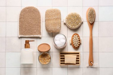 Masaj vücut fırçaları, sabun çubuğu, pamuk topları ve beyaz karo arka planda bir şişe kozmetik ürünü.