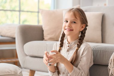 Bir bardak suyla evde oturan sevimli küçük kız.