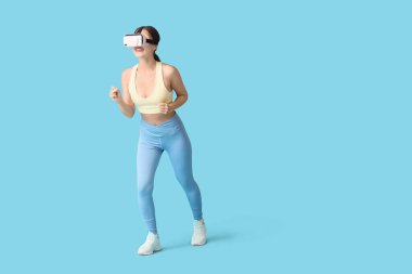 Mavi arka planda koşan VR gözlüklü genç bir kadın.