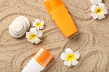 Güneş kremi şişeleriyle Plumeria çiçekleri ve kumdaki spa taşları