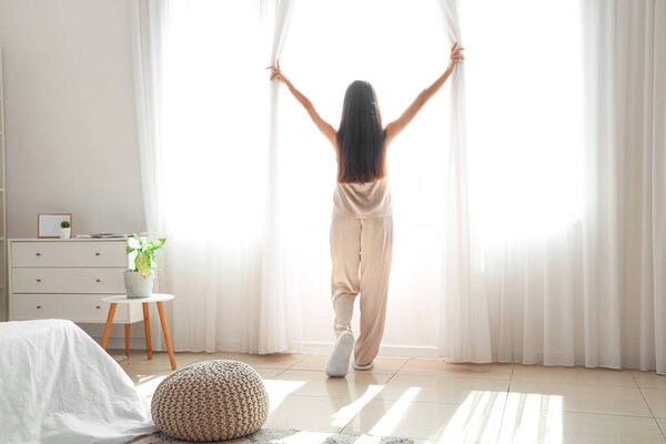 Утро красивой молодой женщины, открывающей шторы в спальне