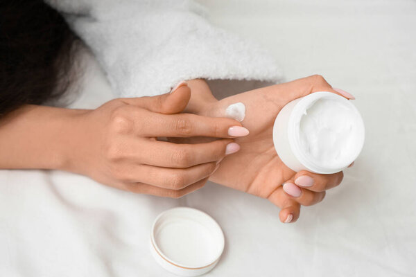 Руки женщины с банкой натурального крема на легкой кровати, крупным планом