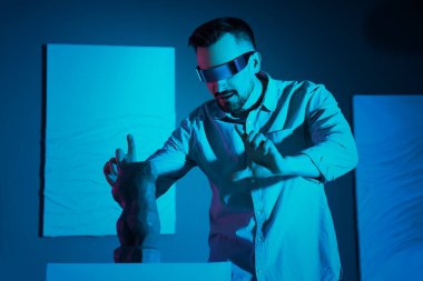 Sanat galerisindeki heykelciğin yanında VR gözlüğü kullanan genç adam.