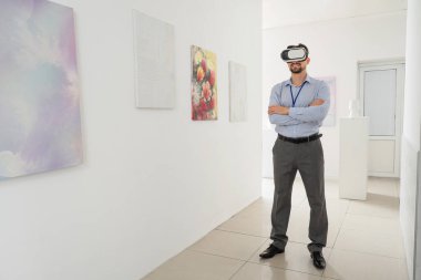 Sanat galerisindeki resimlerin yanında VR gözlüklü genç adam.
