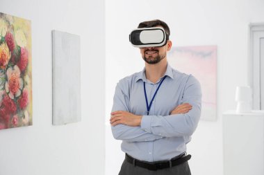 Sanat galerisindeki resimlerin yanında VR gözlüklü genç adam.
