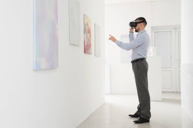 Sanat galerisindeki resimlere bakan VR gözlüklü genç adam.