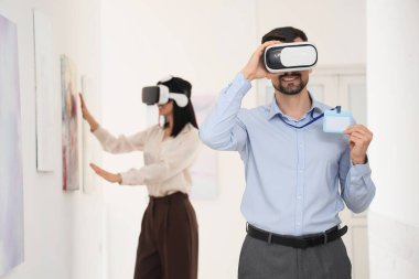 Sanat galerisinde gözlüklü ve rozetli genç bir adam.