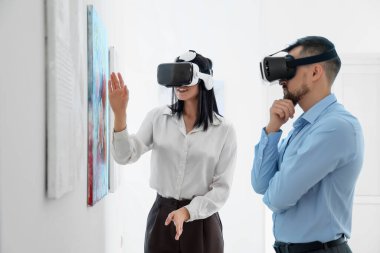 Sanat galerisinde gözlüklü genç bir çift resimlere bakıyor.