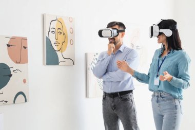 Sanat galerisinde gözlüklü genç bir çift resimlere bakıyor.