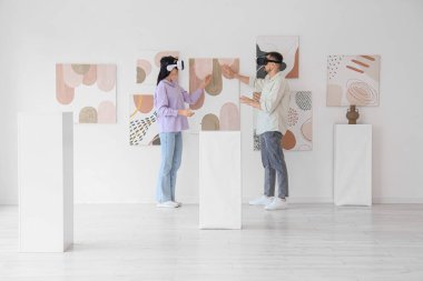 Modern sanat galerisindeki resimlerin yanında VR gözlüklü genç bir çift.
