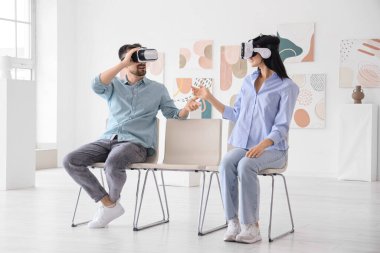 Sanal gerçeklik gözlüklü genç çift modern sanat galerisinde sandalyede konuşuyor.