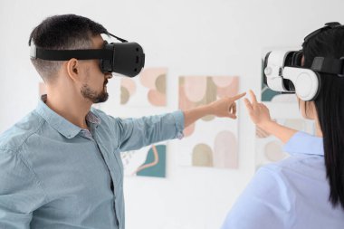 Sanal gerçeklik gözlüklü genç çift modern sanat galerisinde resimlere bakıyor.