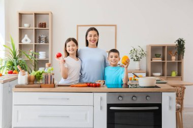 Genç anne çocuklarına mutfakta sebzelerle sarılıyor.