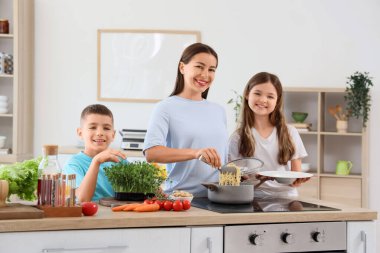 Genç anne ve çocukları mutfaktaki lezzetli makarnayı tabağa koyuyorlar.
