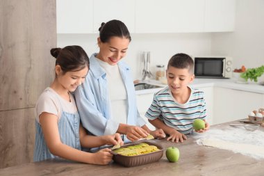 Genç anne ve çocukları mutfakta elmalı turta yapıyor.