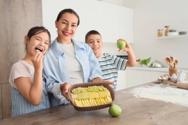 Genç anne ve çocukları mutfakta elmalı turta yapıyor.