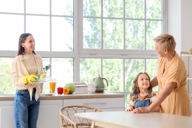 Annesi ve büyükannesiyle birlikte mutfakta bulaşık yıkayan küçük bir kız.