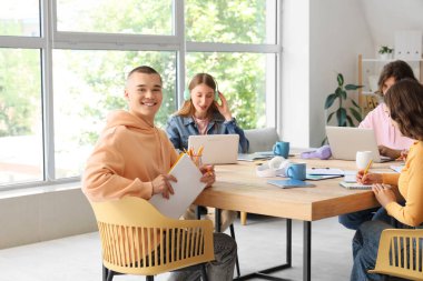 Erkek öğrenci sınıfta sınıf arkadaşlarıyla birlikte ders çalışıyor.