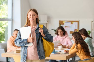 Sınıfta sırt çantası ve dizüstü bilgisayarı olan bir kız öğrenci var.