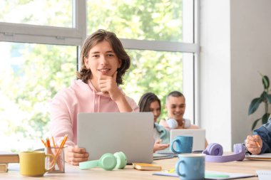 Erkek öğrenci sınıfta dizüstü bilgisayarla çalışıyor.