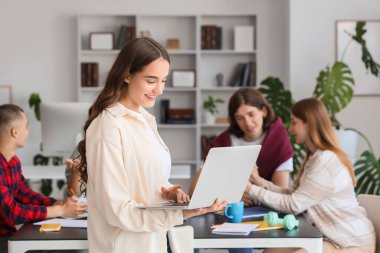 Kütüphanede sınıf arkadaşlarına karşı dizüstü bilgisayarla çalışan kız öğrenci