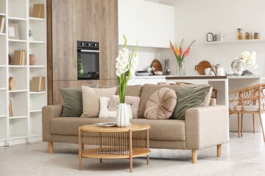 Mutfağın içinde kanepe, kitaplık ve vazolarda gladyatör çiçekleri var.