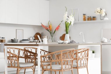 Mutfağın içinde masa, tezgah ve vazolarda gladyatör çiçekleri var.