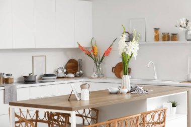 Mutfağın içinde masa, tezgah ve vazolarda gladyatör çiçekleri var.