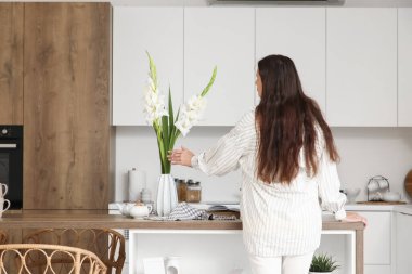 Mutfaktaki masada gladiolus çiçekleri olan genç bir kadın ve vazo.