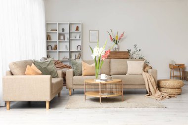 Oturma odasının içinde kanepeler, masa ve vazolarda gladyatör çiçekleri.