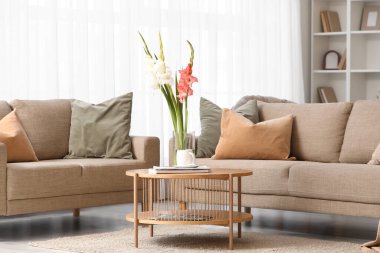 Oturma odasının içinde kanepeler, masa ve gladyatör çiçekleri var.