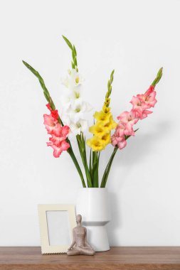Gladiolus çiçekli vazo, heykelcik ve boş çerçeve ışık duvarının yanında.