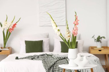 Yatak odasındaki masasında gladiolus çiçekleri olan vazolar.