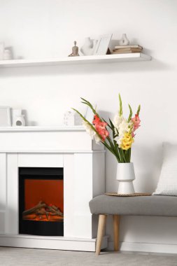 Oturma odasındaki şöminenin yanındaki yumuşak bankta gladiolus çiçekli vazo.