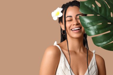 Plumeria çiçeği ve bej arka planda palmiye yaprağı olan güzel Afro-Amerikalı kadın, yakın plan.