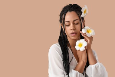 Bej arka planda tesisat çiçekleri olan genç bir Afro-Amerikalı kadın.