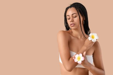 Güzel Afro-Amerikalı kadın bej arka planda tesisat çiçekleri var.