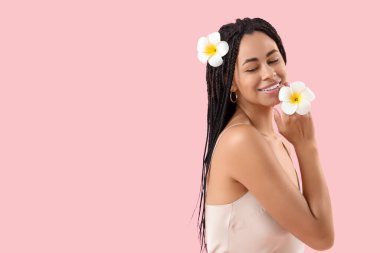 Pembe arka planda çiçekleri olan gülümseyen Afro-Amerikan kadın.