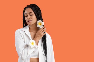 Turuncu arka planda tesisat çiçekleri olan güzel Afro-Amerikalı kadın.