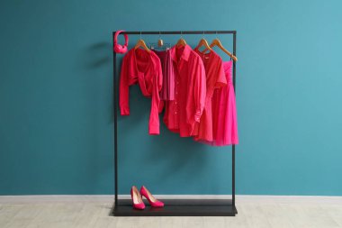 Parlak pembe giysiler, kulaklıklar ve mavi duvarın yanında topuklu ayakkabılar.