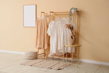 İç kısımda bej duvarın yanında şık kıyafetler var.